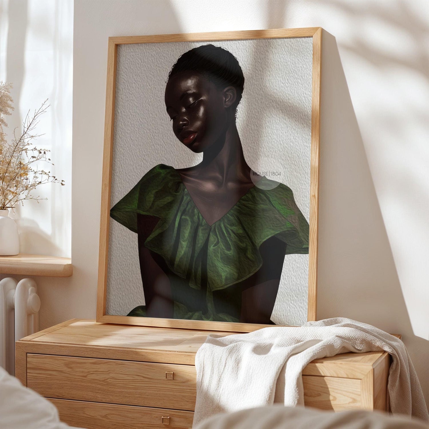 a framed portrait of a woman with a dark skin tone, wearing a green dress, displayed on a wooden dresser.
