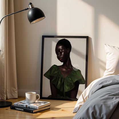 a framed portrait of a woman in a green dress, placed on a wooden floor next to a bed with a gray comforter. There is a lamp and a stack of books on a nearby table.
